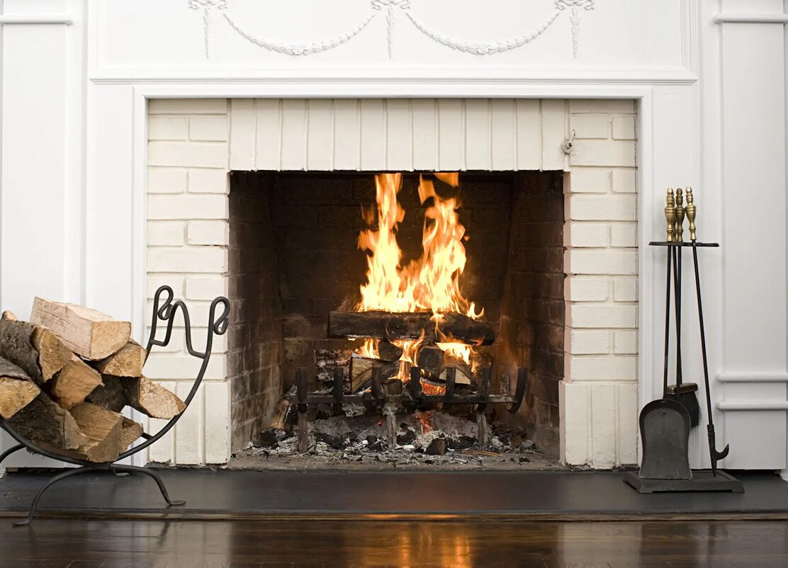 Cozy fireplace with burning logs and tools.